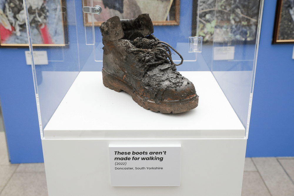 A pair of sewer-found boots on a gallery plinth, labelled 'These boots aren't made for walking'