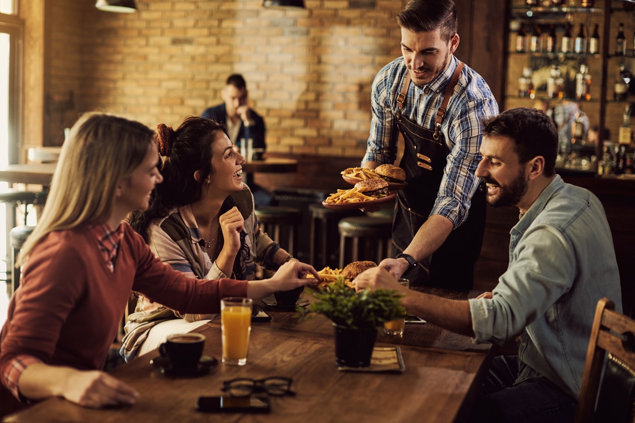 Happy waiter serving food to group of friends in a pub