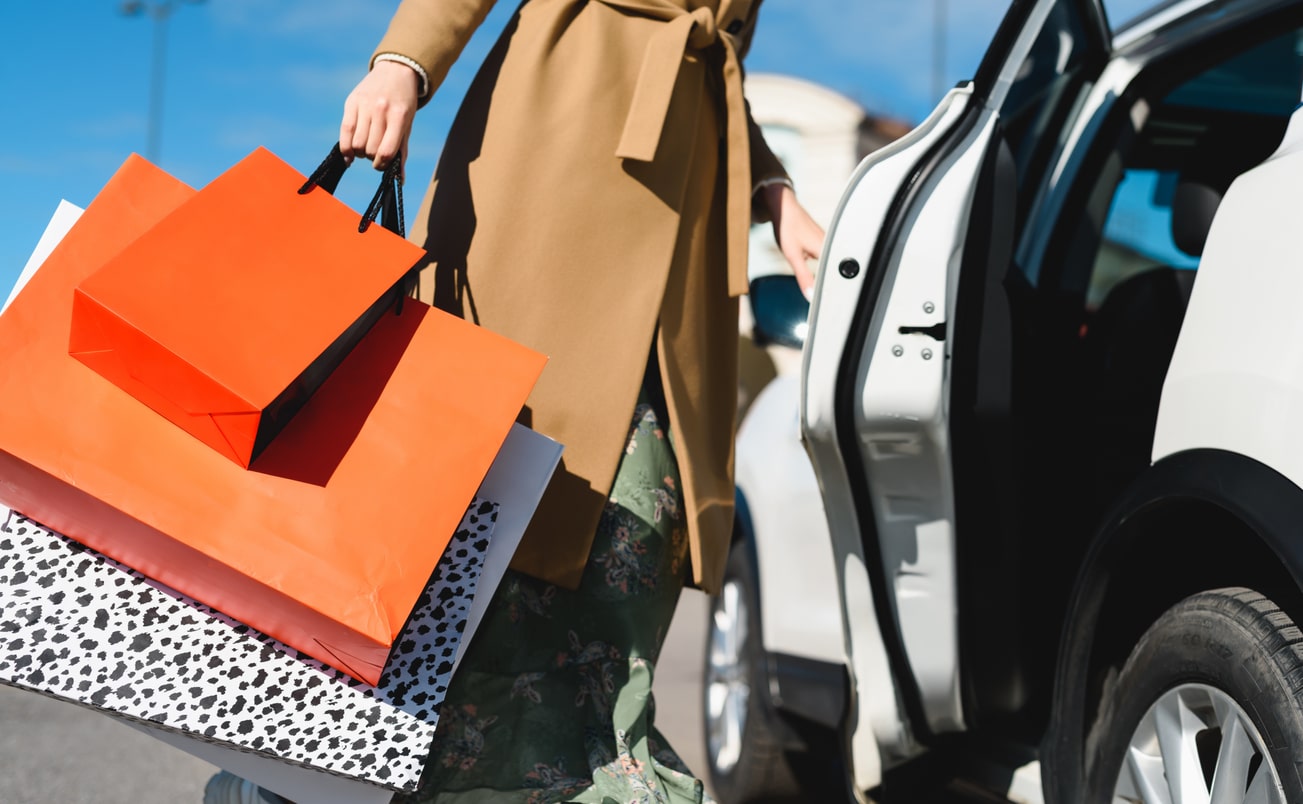 Successful shopping! A woman shopaholic opening the car door to load a lot of packages from different stores