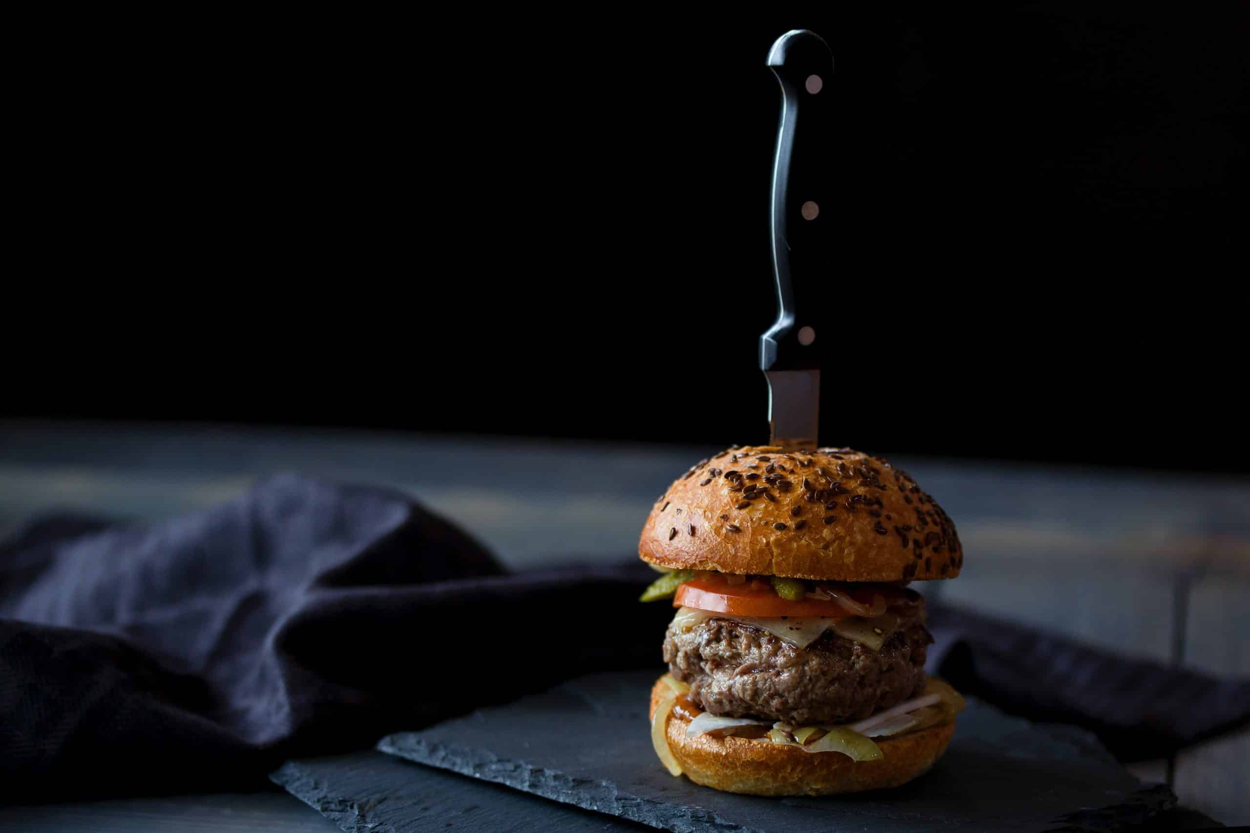 Burger skewered with knife near black textile