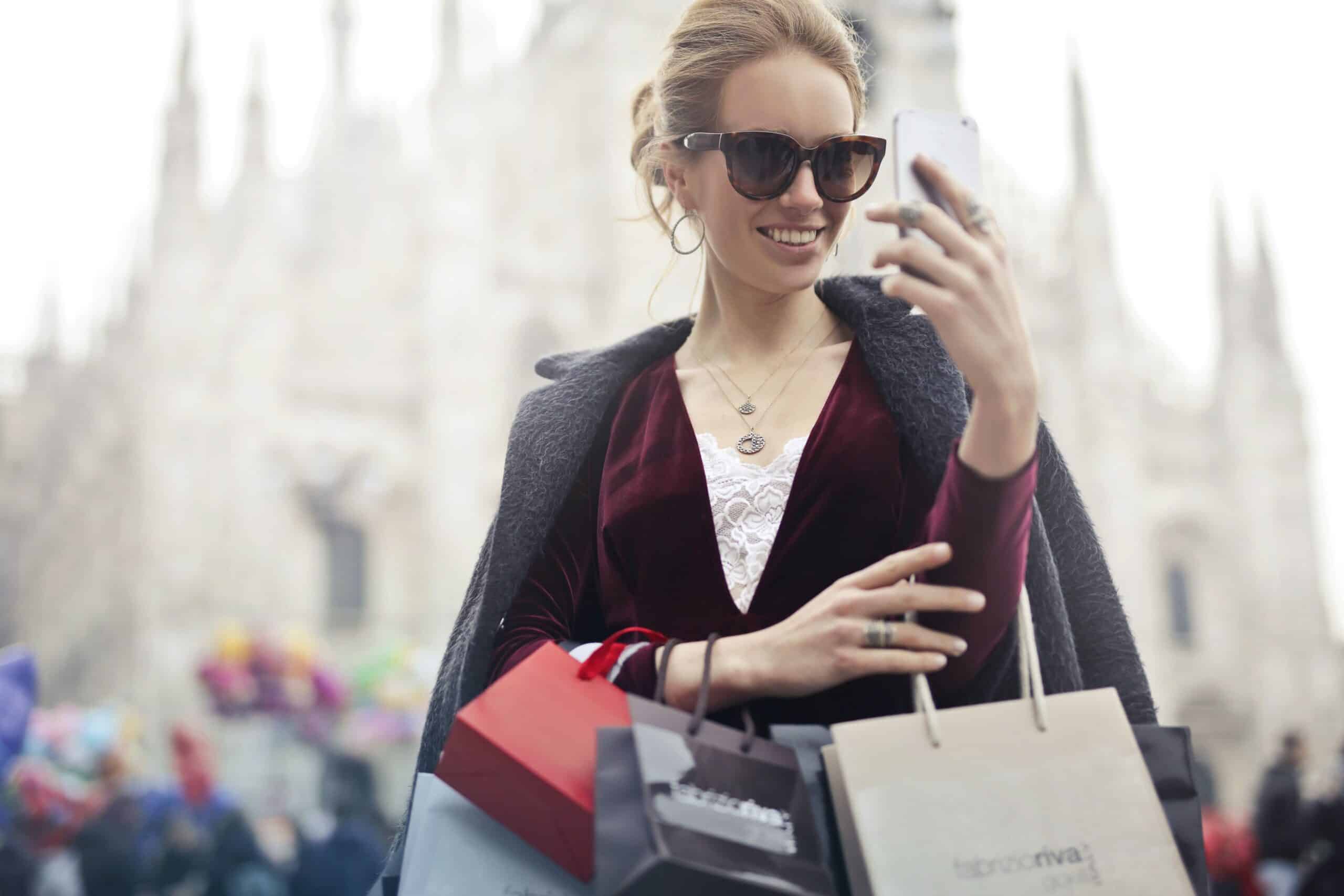 A wealthy shopper taking a selfie with luxury shopping bags, reflecting how personal social sharing shapes brand perception