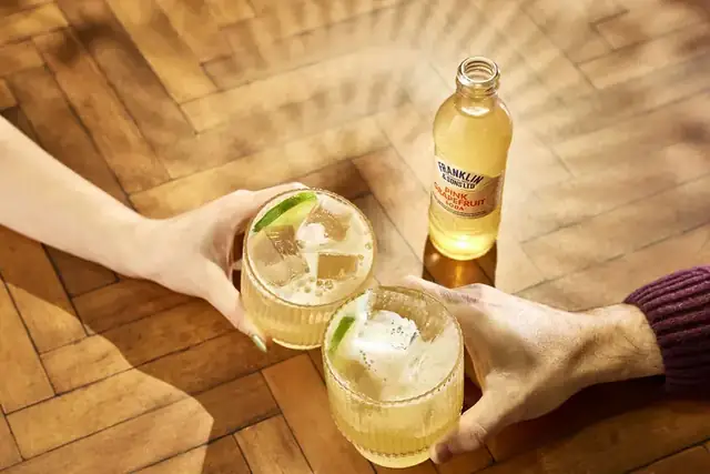 Two hands toasting with Paloma cocktails made with Franklin & Sons Pink Grapefruit Soda
